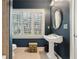 Elegant blue bathroom with white pedestal sink and matching framed round mirror, plus window with stylish white shutters at 963 Manor Parc Dr, Decatur, GA 30033