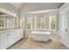 Bright bathroom featuring a standalone tub under natural light with dual marble vanity sinks and shuttered windows at 10000 Groomsbridge Rd, Johns Creek, GA 30022