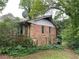 Exterior side view of the home with a brick facade and a small window, surrounded by overgrown yard at 1481 Pine St, Stone Mountain, GA 30087