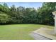Large backyard with healthy grass and a concrete patio, bordered by mature trees and foliage at 237 River Pass Ct, Dacula, GA 30019