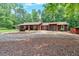 Charming single-story home with a large gravel driveway and surrounded by tall trees and greenery at 712 Honeysuckle Ln, Temple, GA 30179