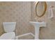 Cozy half-bathroom featuring pedestal sink, oval mirror, and patterned wallpaper at 4047 Watkins Glen Dr, Woodstock, GA 30189