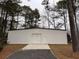 Exterior view of a large metal building with a roll-up door, surrounded by mature trees and gravel driveway at 1445 Hillside Dr, Grayson, GA 30017