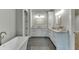 Bright bathroom featuring double sink vanity, soaking tub, white cabinets, and gray tiled floors at 7620 Breeze Bay Rd, Cumming, GA 30041