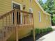 Side view of a yellow home featuring a wooden staircase leading to an open door and manicured bushes along the foundation at 2460 Due West Nw Cir, Kennesaw, GA 30152