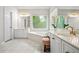 Bright bathroom with white cabinets, gold fixtures, a garden tub, and a large window overlooking greenery at 3944 Blustery Ne Way, Marietta, GA 30066