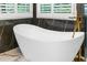 A standalone tub and a gold-colored faucet sit in front of an accent wall and windows with bright light at 230 Leaf Court, Alpharetta, GA 30005