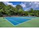 A well-maintained tennis court with a bright blue surface, surrounded by lush greenery and tall trees at 935 Brookline Way, Alpharetta, GA 30022