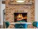 Close-up view of a cozy brick fireplace with a wooden mantel and a small table with blue chairs in front at 7255 Old Rico Rd, Chattahoochee Hills, GA 30268