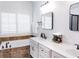 Bright bathroom features a double vanity, soaking tub with tile surround, and shuttered window at 9195 Tuckerbrook Ln, Alpharetta, GA 30022