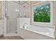 Bright bathroom featuring a shower, large tub, and a window with view of trees outside at 4910 Aldbury Ln, Suwanee, GA 30024