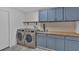 Laundry room features stainless steel washer and dryer with blue cabinets, wood counters, and decor at 1421 Hendon Rd, Woodstock, GA 30188