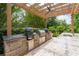Backyard outdoor kitchen has stone counter tops, bar seating, and a built-in grill area under the pergola at 5860 Stoneleigh Dr, Suwanee, GA 30024