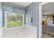 Bright bathroom featuring a jacuzzi tub, blue floral wallpaper, and a window overlooking the backyard at 3472 Honeycomb Se Dr, Conyers, GA 30094