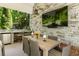 Covered outdoor dining area with a stone wall, TV, mini fridge, and seating for six at 11355 Bowen Rd, Roswell, GA 30075