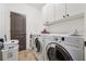 Bright laundry room featuring white washer and dryer with overhead cabinets and tile floor at 5068 Bentwater Sw Ln, Lilburn, GA 30047