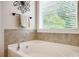 Corner bathroom tub featuring tile surround, brushed fixtures, and a sunlit window view at 122 Grove View Rd, Woodstock, GA 30189