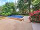 A pool covered with a tarp, a concrete deck, bushes, trees, and a wooden fence surround the area at 6005 Pattingham Dr, Roswell, GA 30075