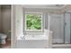 Well-lit bathroom featuring a white tub, a glass-enclosed shower, and a window that offers a view of the outdoors at 3962 Coventry Park Ln, Peachtree Corners, GA 30096