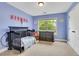 Light blue Bedroom featuring a crib, dresser, and large window with natural light at 1411 Primrose Park Rd, Sugar Hill, GA 30518