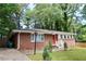 Inviting brick home featuring a red door, surrounded by a green lawn and mature trees, with trash bins on the side at 579 Kenridge Cir, Stone Mountain, GA 30083