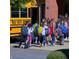 Children with backpacks exiting a yellow school bus in front of a red brick schoolhouse at 5620 Moresby Ct, Alpharetta, GA 30022
