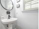 Charming powder room featuring a pedestal sink, round mirror, and a window for natural lighting at 1037 Panoramic Pte, Buford, GA 30518