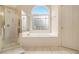 Bathroom featuring a large tub under an arched window, glass shower and tile flooring at 4045 Bonnett Creek Ln, Hoschton, GA 30548
