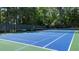 Outdoor tennis court with blue surface surrounded by mature trees and a black net fence at 235 Foxley Way, Roswell, GA 30075