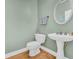 Bathroom featuring white pedestal sink, round mirror, toilet, and wood floors at 1213 Fairwinds Dr, Loganville, GA 30052