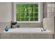 Bathroom tub beneath a large window with green treetop views and tile surround at 1213 Fairwinds Dr, Loganville, GA 30052