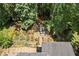 Aerial view of a backyard stone patio with a fire pit, bordered by lush plants and large trees at 580 Washington Way, Cumming, GA 30040