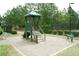 Community playground featuring a green playset with a slide and stairs, surrounded by gravel and lush landscaping at 4020 Alligator Pt, Cumming, GA 30028