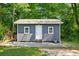 A gray outbuilding with a white door and window is nestled in the greenery of the yard at 100 Chadwick Pl, Villa Rica, GA 30180