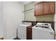 Efficient laundry room equipped with a washer, dryer, storage shelf and overhead cabinet at 9507 Greens Mill Ct, Loganville, GA 30052