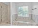 Bright bathroom featuring a jacuzzi tub and shower with a window and marble tiling at 2702 Moorings Pkwy, Snellville, GA 30039