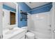 Bright bathroom with white tub, sink, toilet and cool blue paint with custom shelving at 2595 Glaramara Ter, Cumming, GA 30041