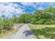 Gravel driveway with a white fence leading to a secluded property amidst lush greenery and a vibrant blue sky at 379 Bohannon Rd, Grantville, GA 30220