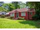 Red brick house with a green lawn, featuring mature trees and decorative front door at 3020 Washington Rd, East Point, GA 30344