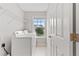 Functional laundry room with white appliances, wire shelving, and a window offering natural light and outdoor views at 8750 Radford Ln, Suwanee, GA 30024