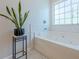 Soaking tub with white tile surround, modern fixtures and a geometric planter near a window at 2304 Mitford Ct, Dacula, GA 30019