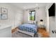 Cozy bedroom with a blue floral bedspread, white walls, hardwood floors, and a window overlooking lush greenery at 819 Belgrade Ne Ave, Atlanta, GA 30306