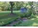Large backyard featuring lush green lawn, mature trees, and a charming detached garage with stone pathway at 4370 Tradition Ter, Austell, GA 30106