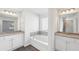 Bathroom with double sinks, granite countertops, and a soaking tub with a window at 11854 Rizvan Pl, Covington, GA 30014