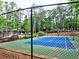 A well-maintained blue and green tennis court enclosed by a fence, with trees and a glimpse of a pool in the background at 2210 Cumberland Se Ct, Smyrna, GA 30080