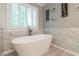 Bright bathroom showcasing a freestanding bathtub with white marble wall tile and a window view at 3394 Floral Ct, Suwanee, GA 30024