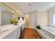 Bright bathroom featuring a jetted tub, white cabinets, a large mirror, and wood flooring at 312 Crabapple Springs Way, Woodstock, GA 30188