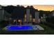 Backyard view of the house with an illuminated blue inground pool and covered patio at dusk at 5440 Old Haven Ct, Cumming, GA 30041