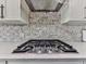 Close-up of a cooktop with stainless steel hood and white stone backsplash and countertops at 603 Canyon Overlook, Canton, GA 30114
