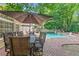 Outdoor dining on the brick patio, shaded by a large umbrella, offering a great view of the pool and green surroundings at 3231 Connemara Trce, Lawrenceville, GA 30044
